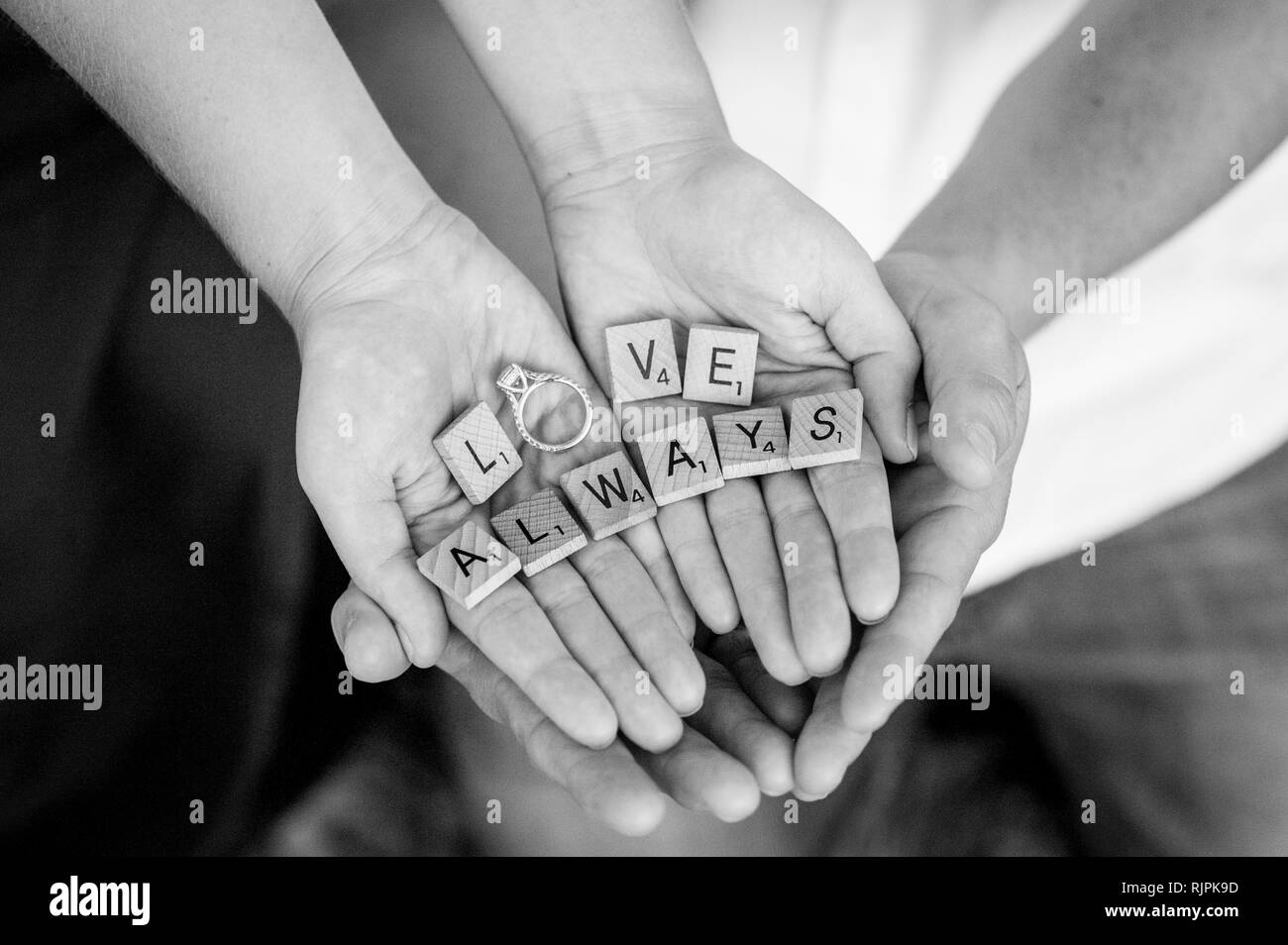 Horizontale Nahaufnahmen der Hände des Verlobten hohle um jeder des anderen, Holding scrabble Stücke Rechtschreibung die Worte "Liebe immer "mit dem Ring. Stockfoto