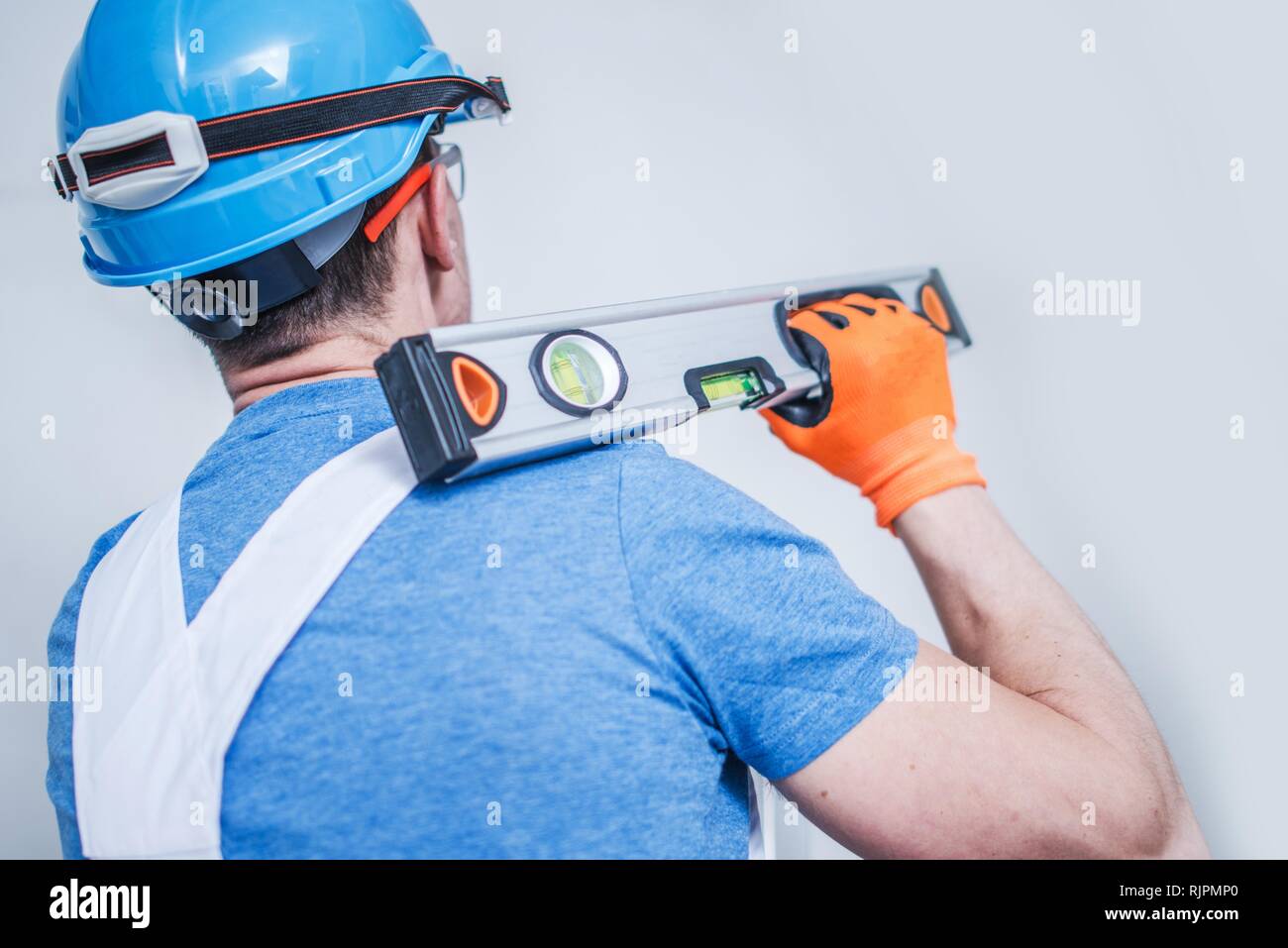 Kaukasische Bauarbeiter mit Wasserwaage Werkzeug auf seiner Schulter. Männer tragen Blaue harten Hut. Stockfoto