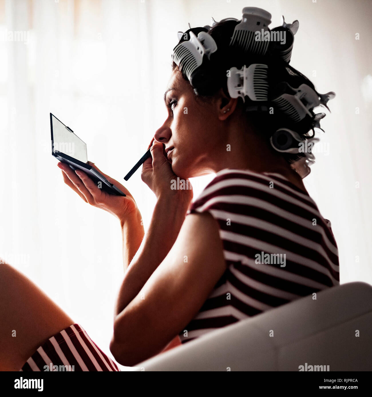 Frau mit Haar-Walzen auf Make-up Stockfoto