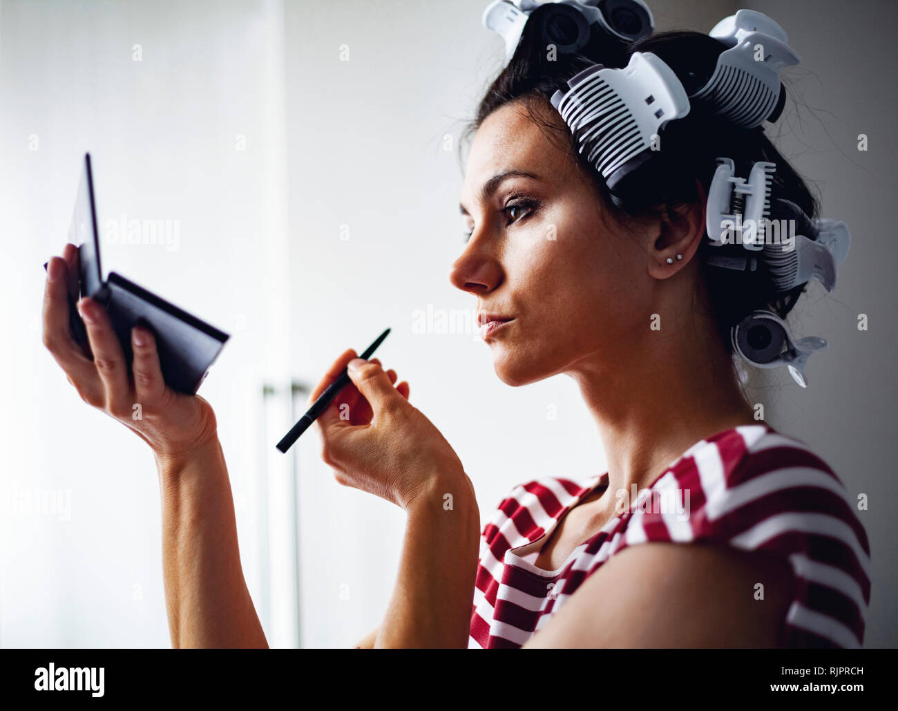 Frau mit Haar-Walzen auf Make-up Stockfoto