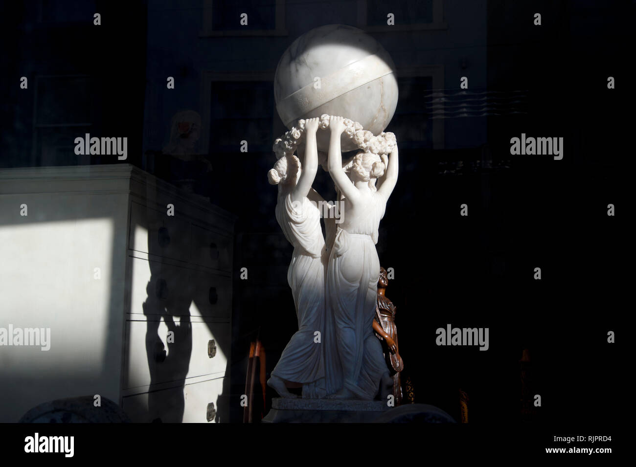 England. Kent. Folkestone. Antique Shop Fenster, Skulptur von drei Frauen einen Ball von der Sonne beleuchtet Stockfoto