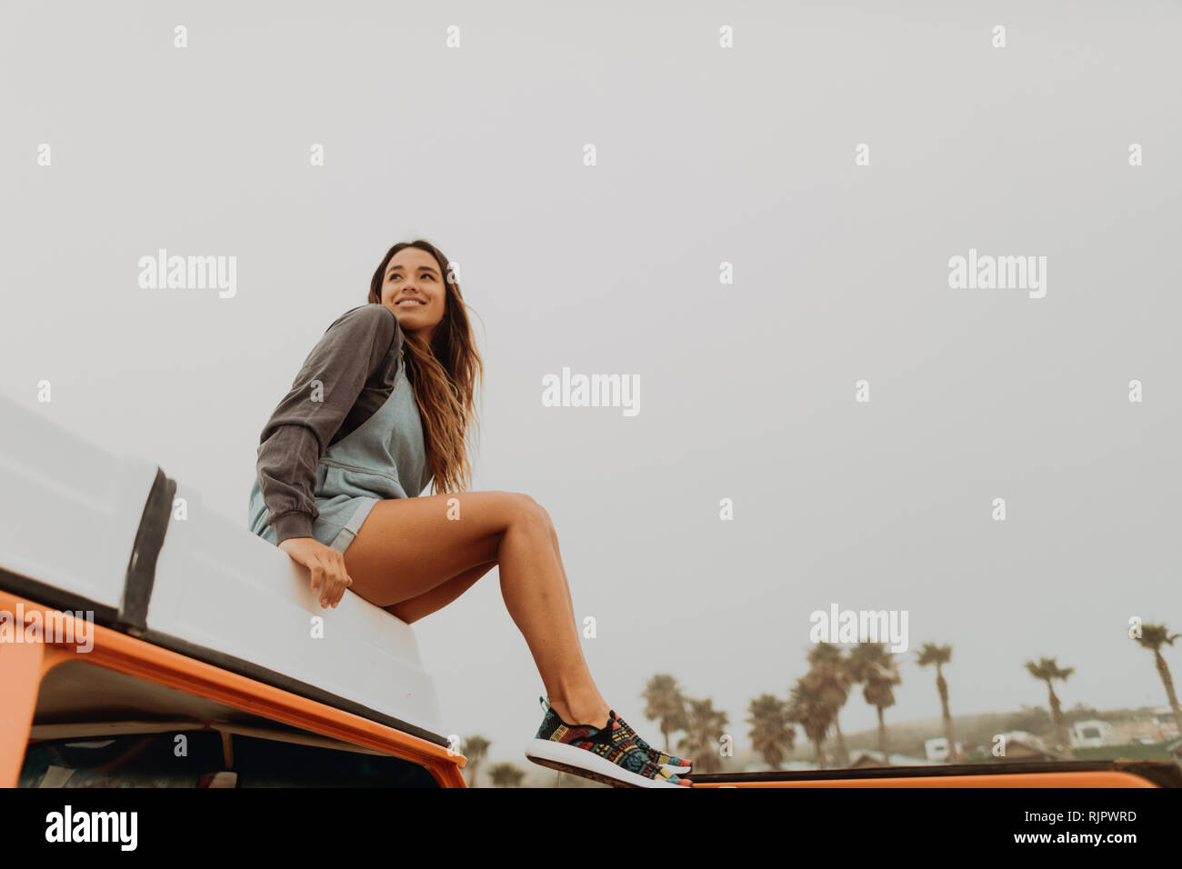 Junge Frau sitzt auf der recreational vehicle Dach am Strand, Jalama, Kalifornien, USA Stockfoto