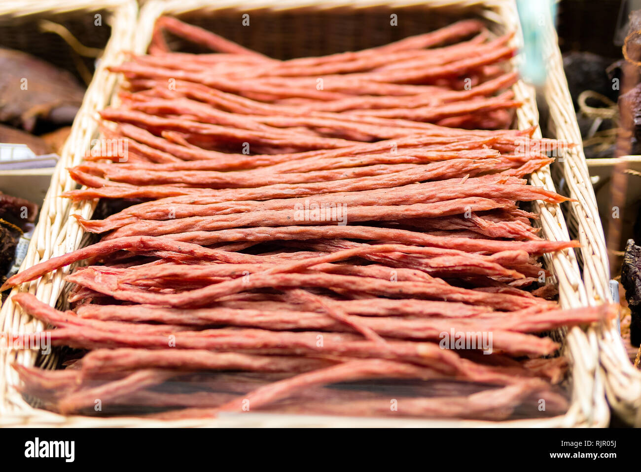 Dünne trockene geräucherte Wurst im Weidenkorb. Kabanossi Wurst. Ansicht von oben Stockfoto