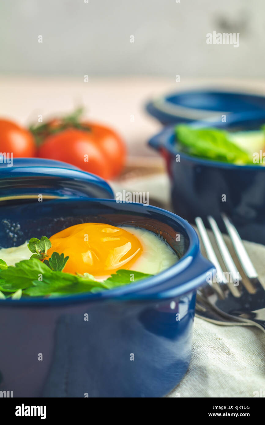 Eier kokot Cocotte französisches Frühstück. Gebackene Eier in blau Keramik Backformen. Portioniert Auflauf aus Gemüse und Eier im italienischen Stil. Nahaufnahme Stockfoto