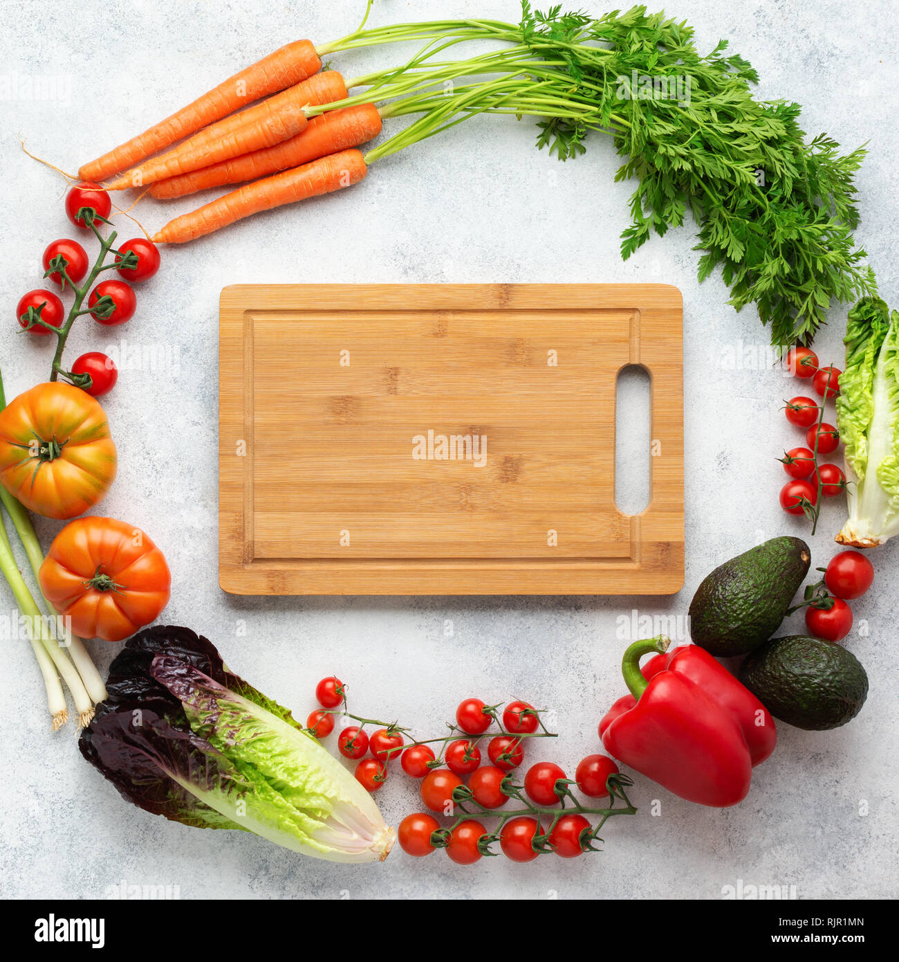 Frische Zutaten in einem Kreis angeordnet mit Schneidebrett in der Mitte, Tomaten Salat Pfeffer avocado Karotten auf dem weißen Tabelle, Ansicht von oben, selektiver Fokus Stockfoto