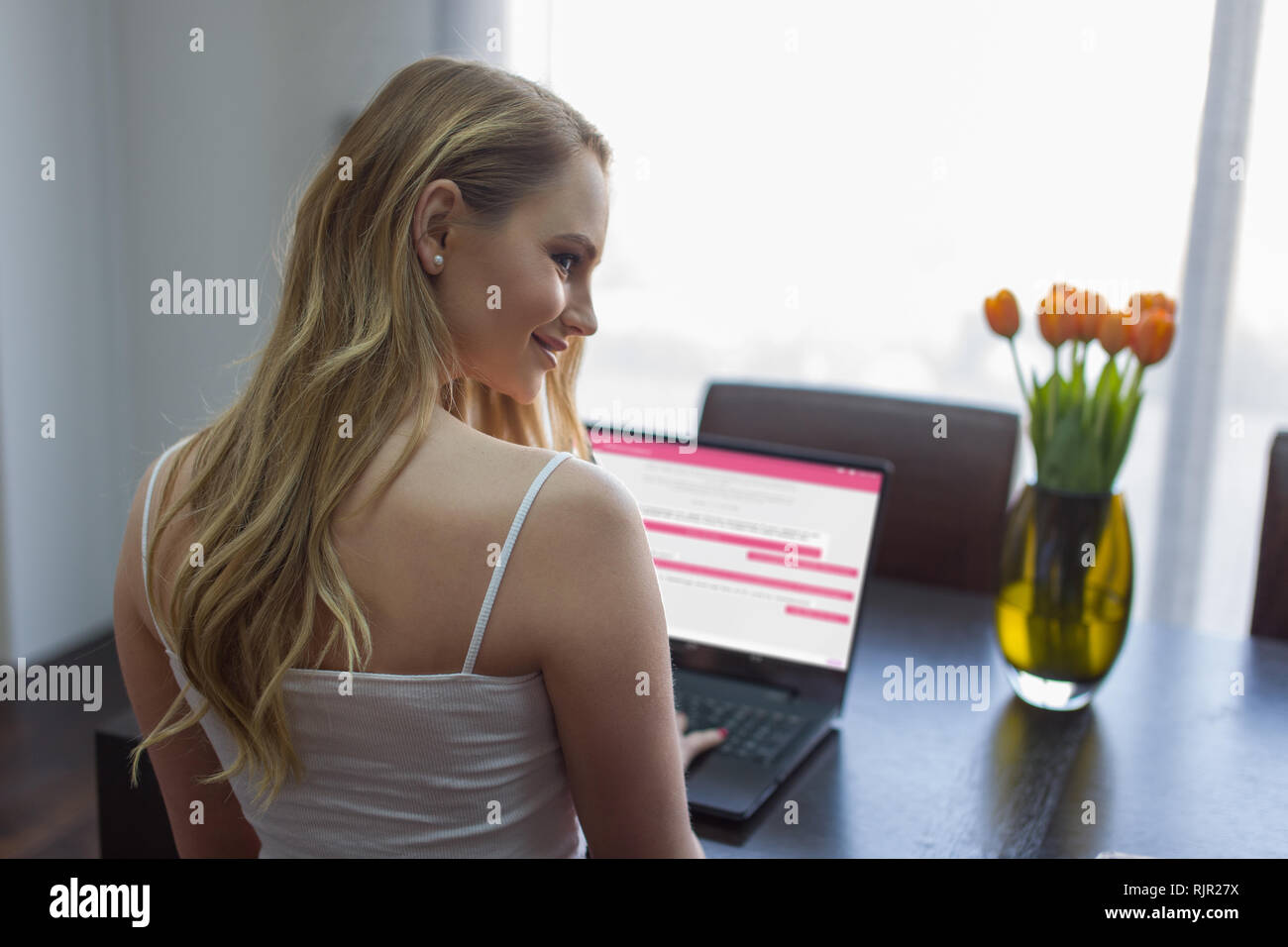 Junge Frau online Chat auf Laptop zuhause über die Schulter schauen Stockfoto