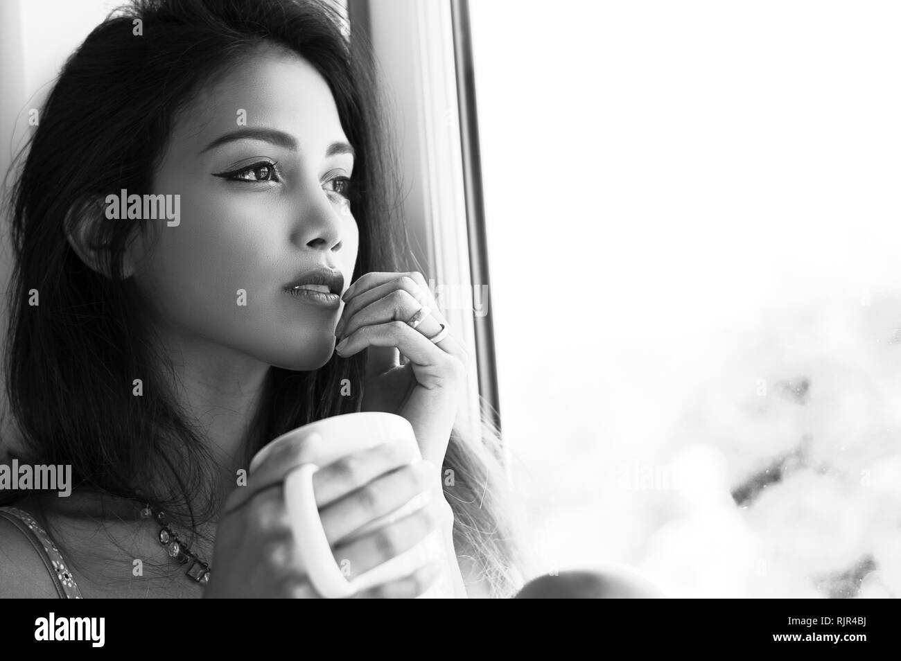 Ein Portrait von einer attraktiven Frau sitzt im Fenster das Trinken einer Tasse Kaffee Stockfoto