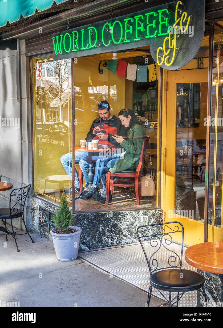 ASHEVILLE, NC, USA-2/3/19: Ein Paar sitzt vor Schaufenster der Coffee Shop, am kleinen Tisch, jeder auf Smartphones. Stockfoto