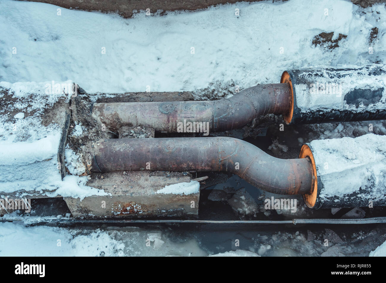 Zwei geschweißte Stahlrohre mit Isolierung in einem schneebedeckten Graben mit etwas Wasser in den Boden Stockfoto