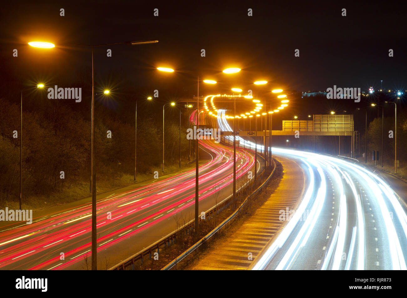 Lange Reihe von Niederdruck-Natriumstraßenlampen auf der Autobahn M60 in der Nähe von Stockport in Richtung Norden. Leichte Spuren, Wiederholung, Muster. Straße in Großbritannien Stockfoto