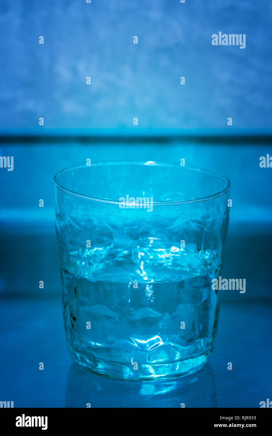 Handgemachte Glas mit Wasser vor einem blauen Hintergrund, halb voll. Konzeptuelle Serie: 2/3 (voll, halb voll, leer). Stockfoto