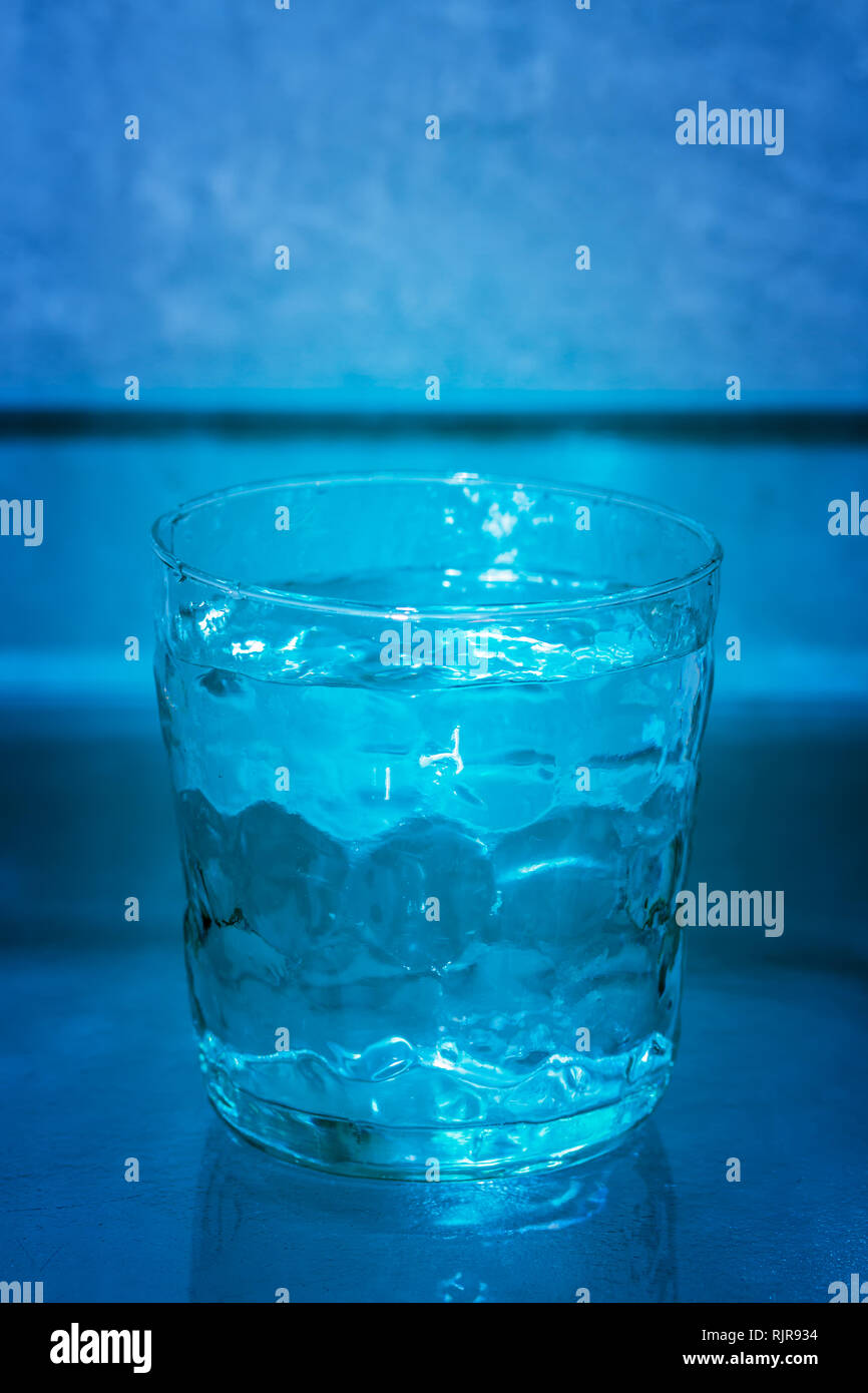 Handgemachte Glas mit Wasser vor einem blauen Hintergrund, voll. Konzeptuelle Serie: 1/3 (voll, halb voll, leer). Stockfoto