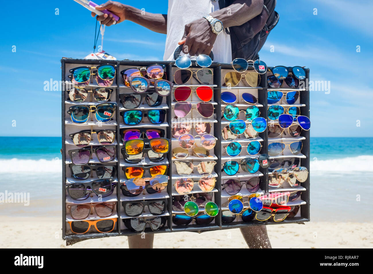 RIO DE JANEIRO - Januar, 2017: Eine afrikanische Einwanderer Verkauf gefälschter Sonnenbrille geht mit einer Vitrine auf der Suche nach Kunden am Strand von Ipanema. Stockfoto