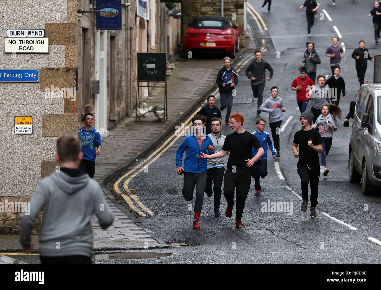 Boys laufen mit dem Lederball eine Seitenstraße entlang während des jährlichen "Fastern's E'en Hand Ba" Events auf Jedburgh's High Street in den Scottish Borders. Stockfoto