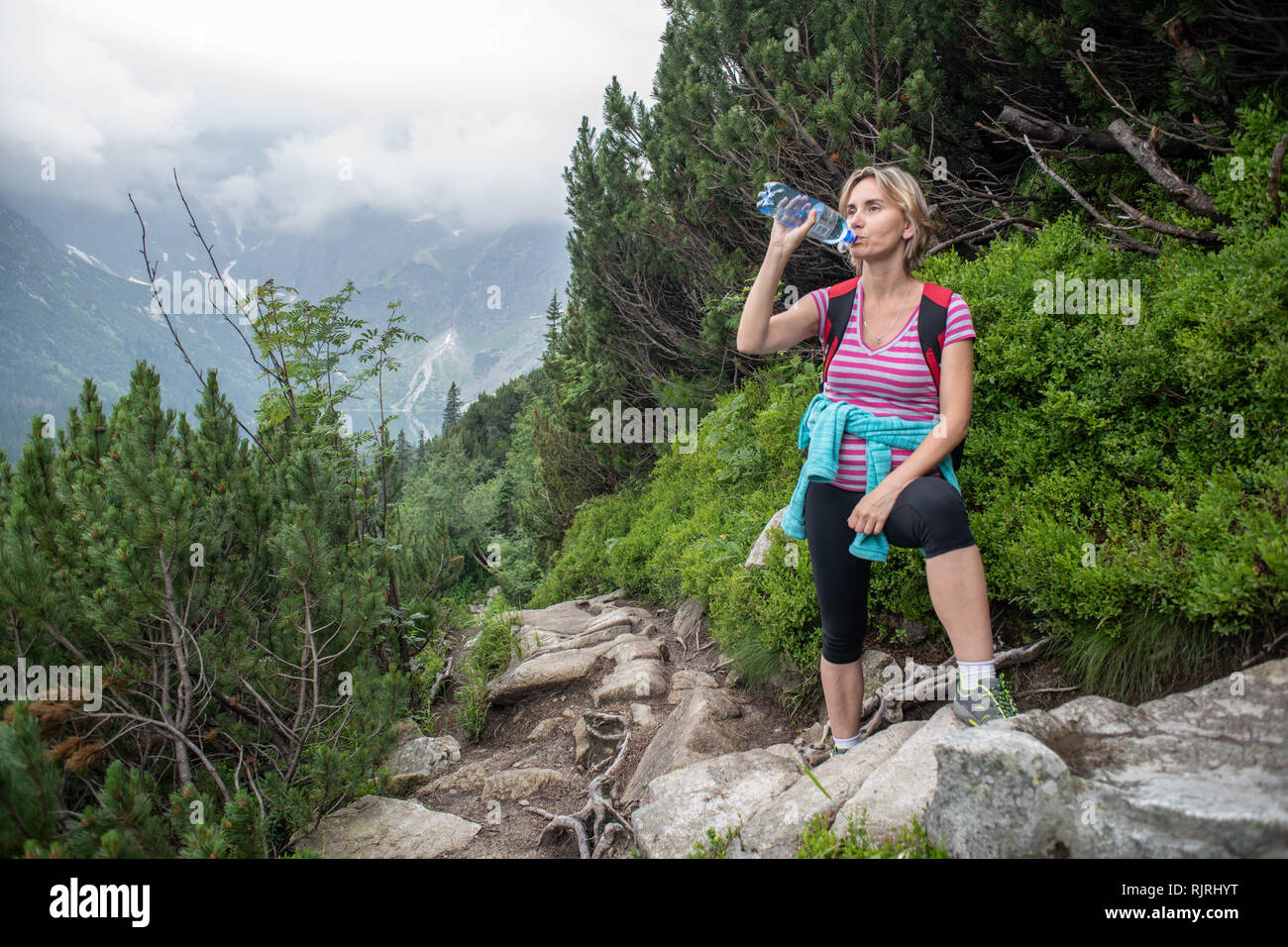 Eine Frau kommt für ein Wasser Pause auf einem felsigen Trail in den Bergen der Hohen Tatra in der Tatra Nationalpark, Woiwodschaft Kleinpolen, Polen. Stockfoto