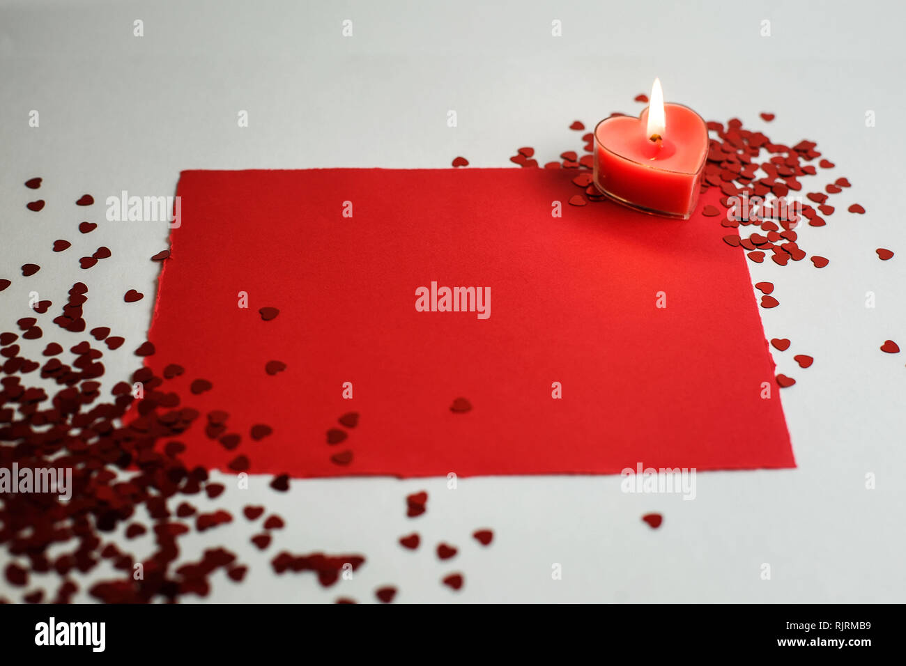 Herzförmige Kerze auf einem weißen Hintergrund unter den kleinen roten Herzen. Guter Hintergrund für den Valentinstag oder Hochzeit Stockfoto