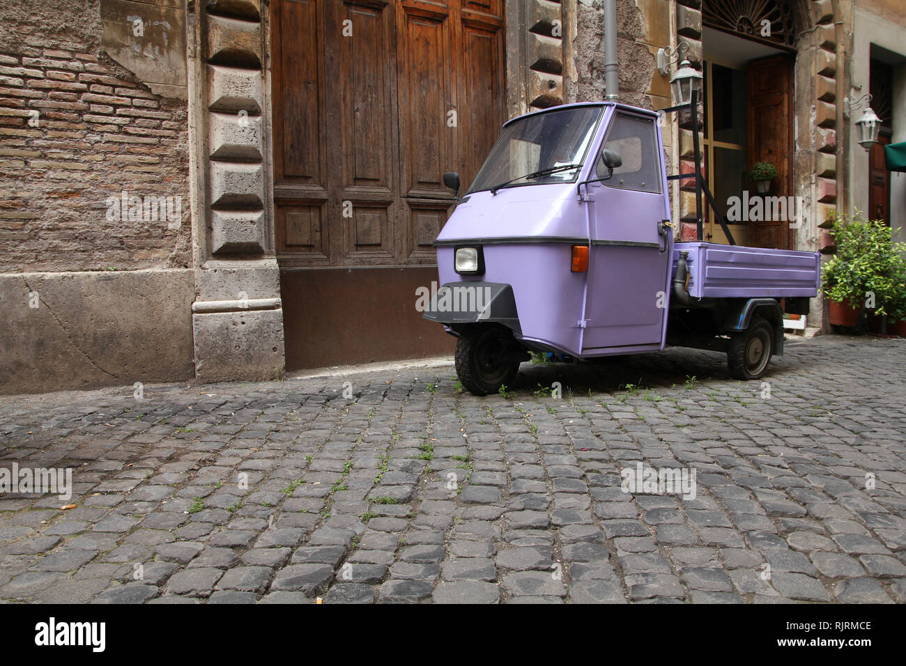 Rom, Italien. Straße mit Kopfsteinpflaster und einem witzigen dreirädrigen Auto. Stockfoto