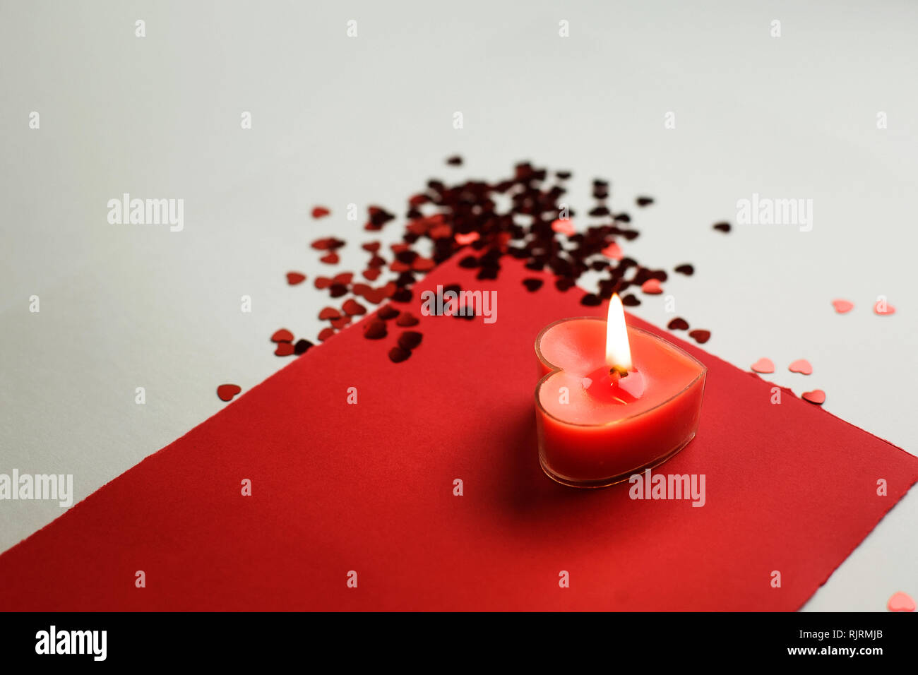 Herzförmige Kerze auf einem weißen Hintergrund unter den kleinen roten Herzen. Guter Hintergrund für den Valentinstag oder Hochzeit Stockfoto