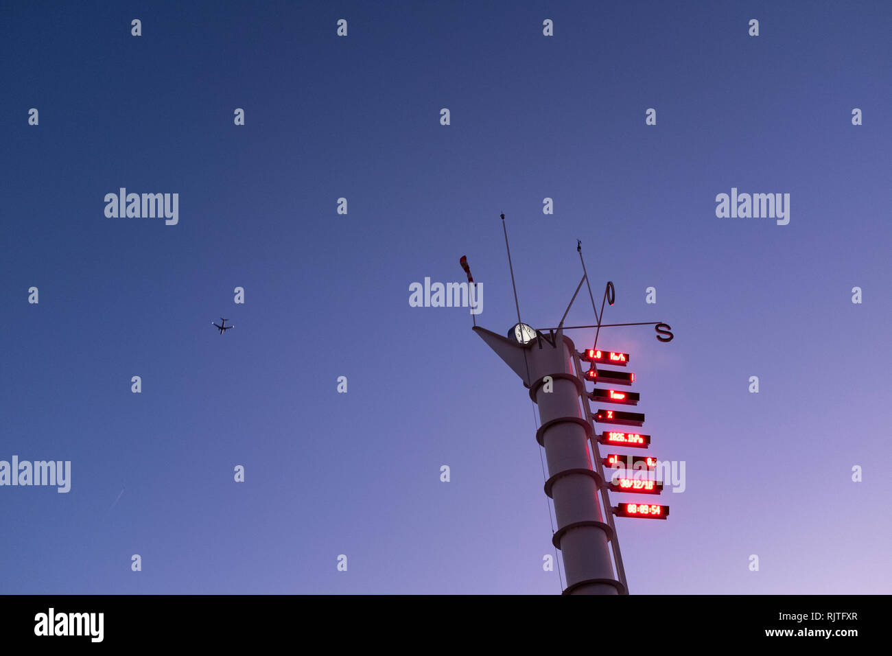 Wetter Vene und Uhrturm mit digitaler Temperaturanzeige gegen den strahlend blauen Himmel Dawn mit einem Flugzeug über fliegende Silhouette Stockfoto