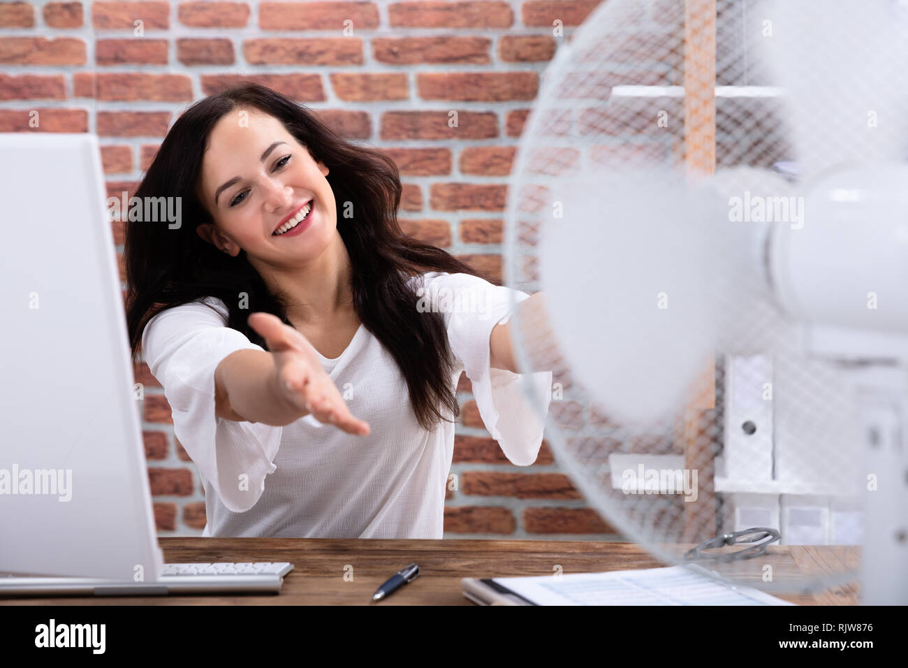 Gerne Reife Geschäftsfrau kühlen sich mit elektrischen Lüfter am Arbeitsplatz am Schreibtisch aus Holz Stockfoto