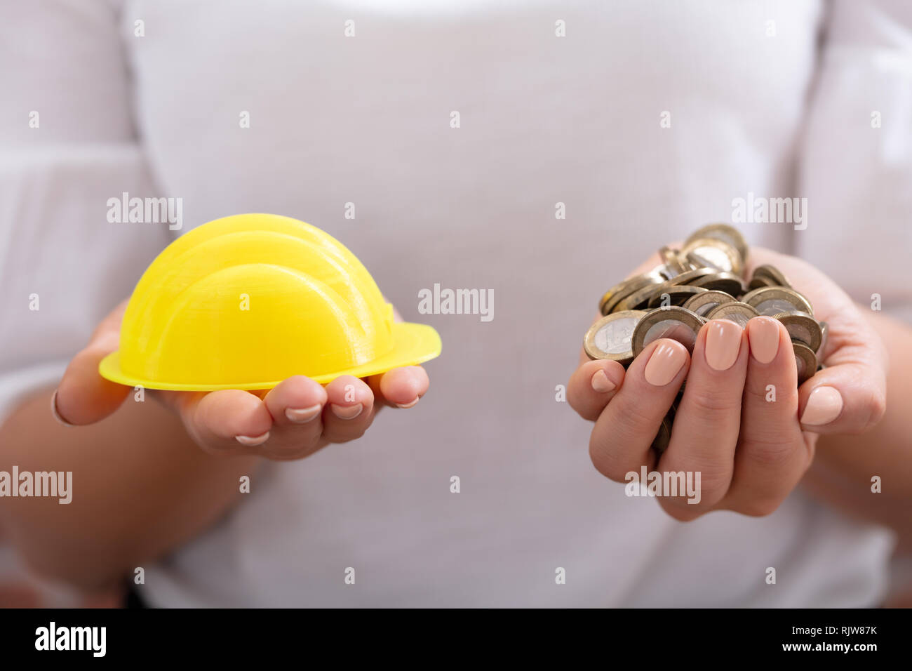 Nahaufnahme einer Hand, die eine Gelbe einer Person hardhat und goldenen Münzen Stockfoto