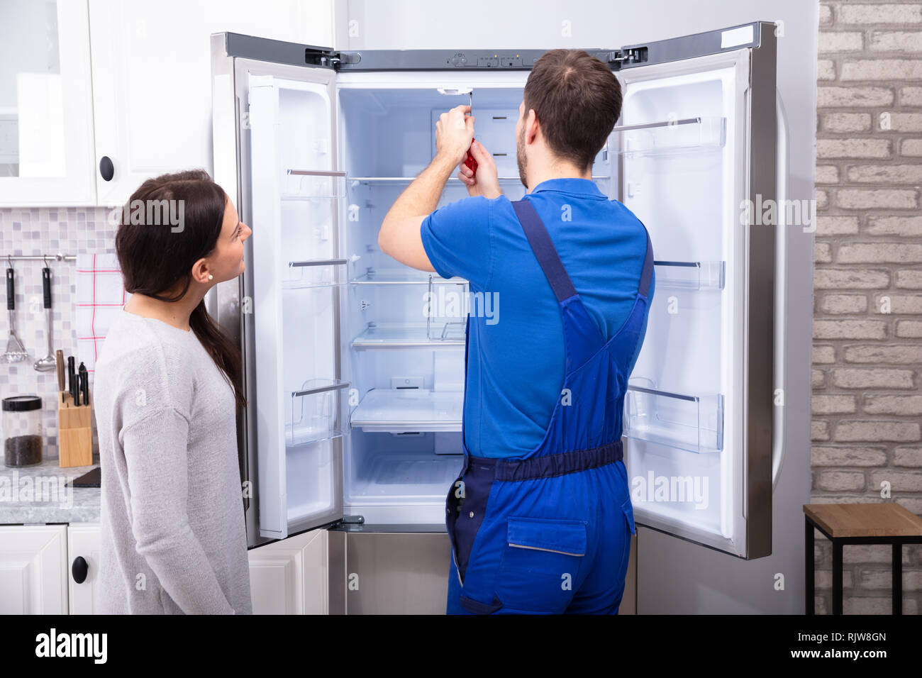 Frau auf der Suche nach männlichen Handwerker zur Festsetzung Kühlschrank mit Schraubendreher Stockfoto