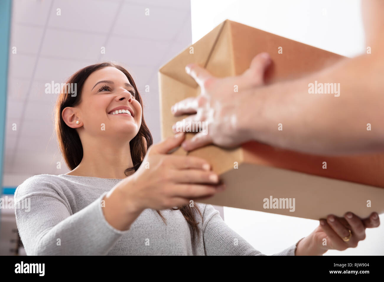 Glückliche junge Frau akzeptieren Karton ab Lieferung Mann Stockfoto