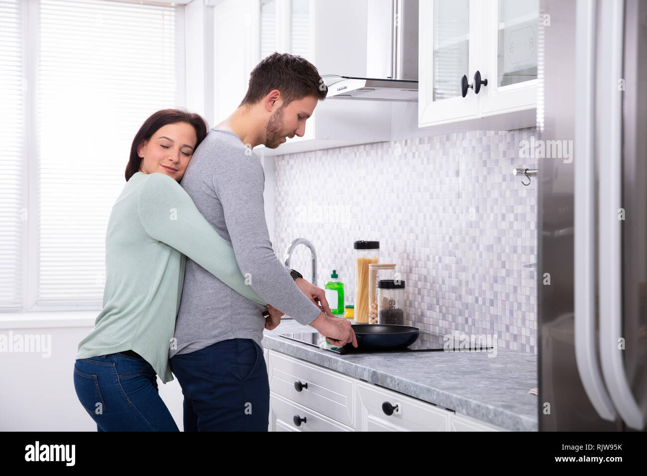 Junge Mann macht Essen mit seinem lächelnden Frau steht in der Küche Stockfoto
