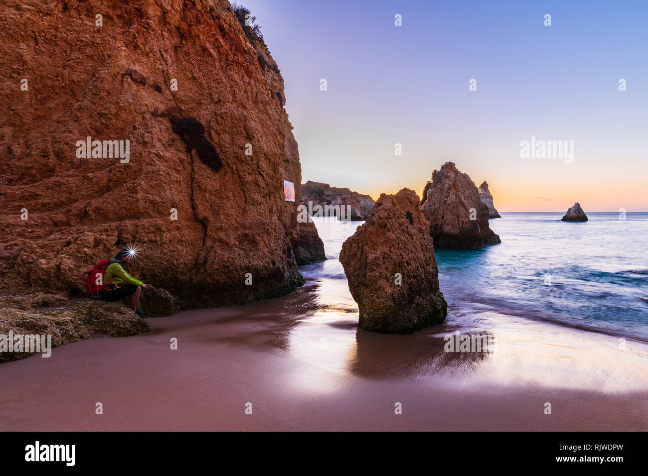 Mann sitzt von Cliff mit beleuchteten Scheinwerfer, Alvor, Algarve, Portugal, Europa Stockfoto