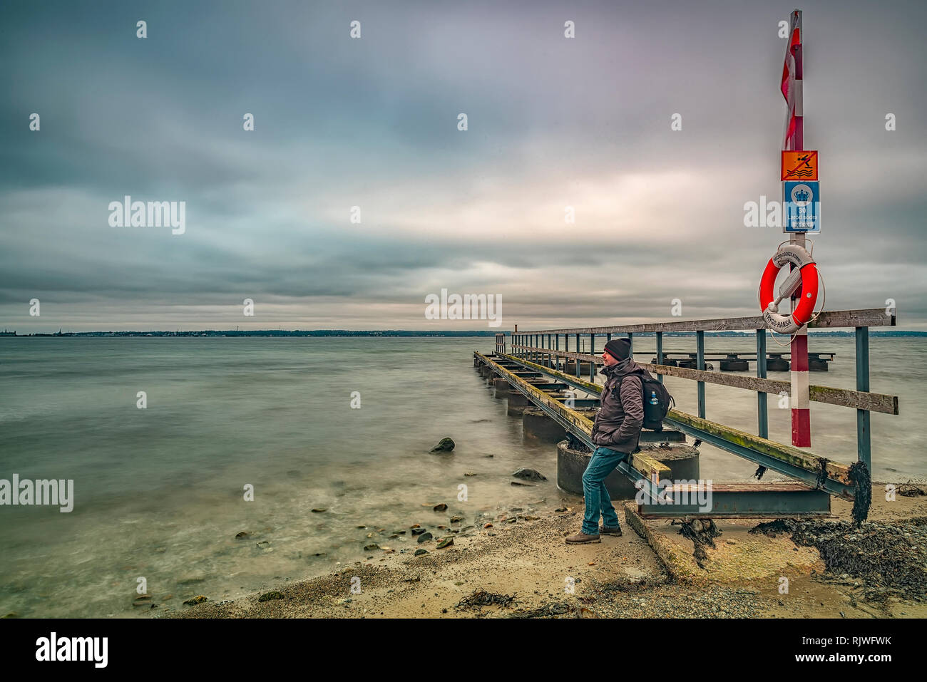 LAROD, Schweden - Februar 03, 2019: Ein altes Pier auf Larod Strand außerhalb von Helsingborg mit einem Mann mit Blick auf den Öresund in Richtung Dänemark. Stockfoto