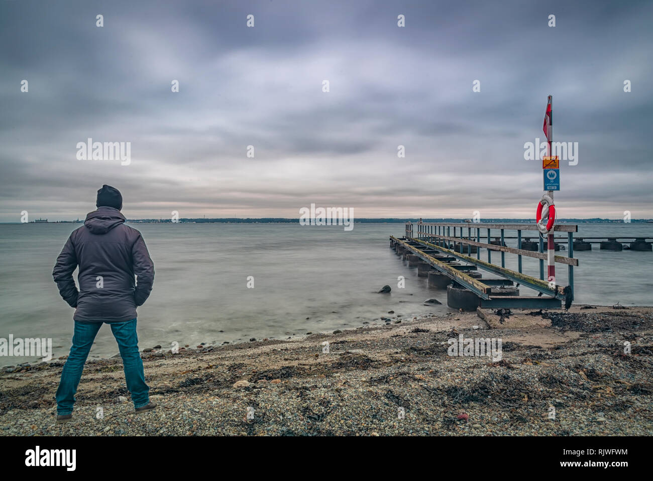 LAROD, Schweden - Februar 03, 2019: Ein altes Pier auf Larod Strand außerhalb von Helsingborg mit einem Mann mit Blick auf den Öresund in Richtung Dänemark. Stockfoto