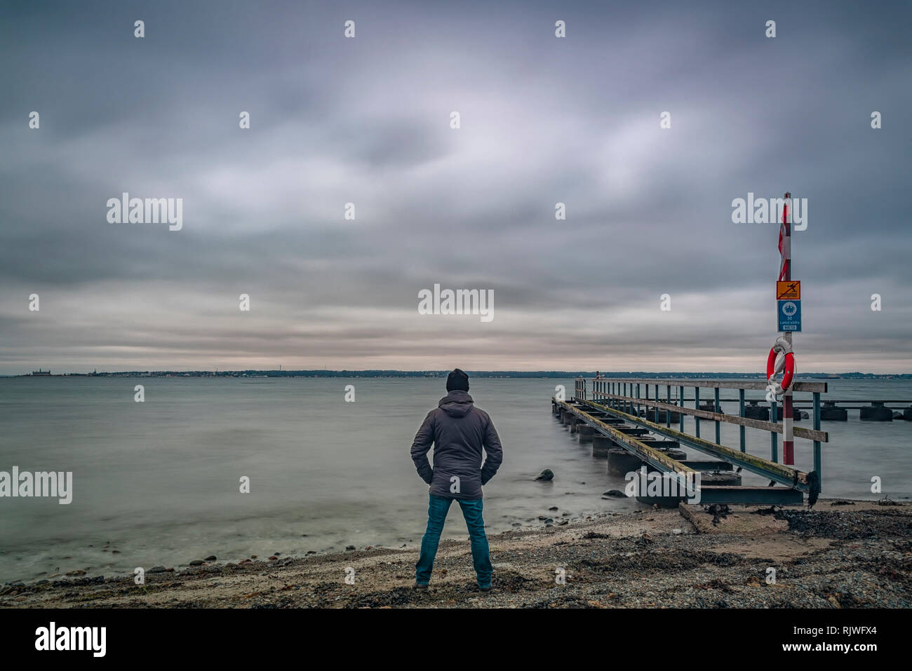 LAROD, Schweden - Februar 03, 2019: Ein altes Pier auf Larod Strand außerhalb von Helsingborg mit einem Mann mit Blick auf den Öresund in Richtung Dänemark. Stockfoto