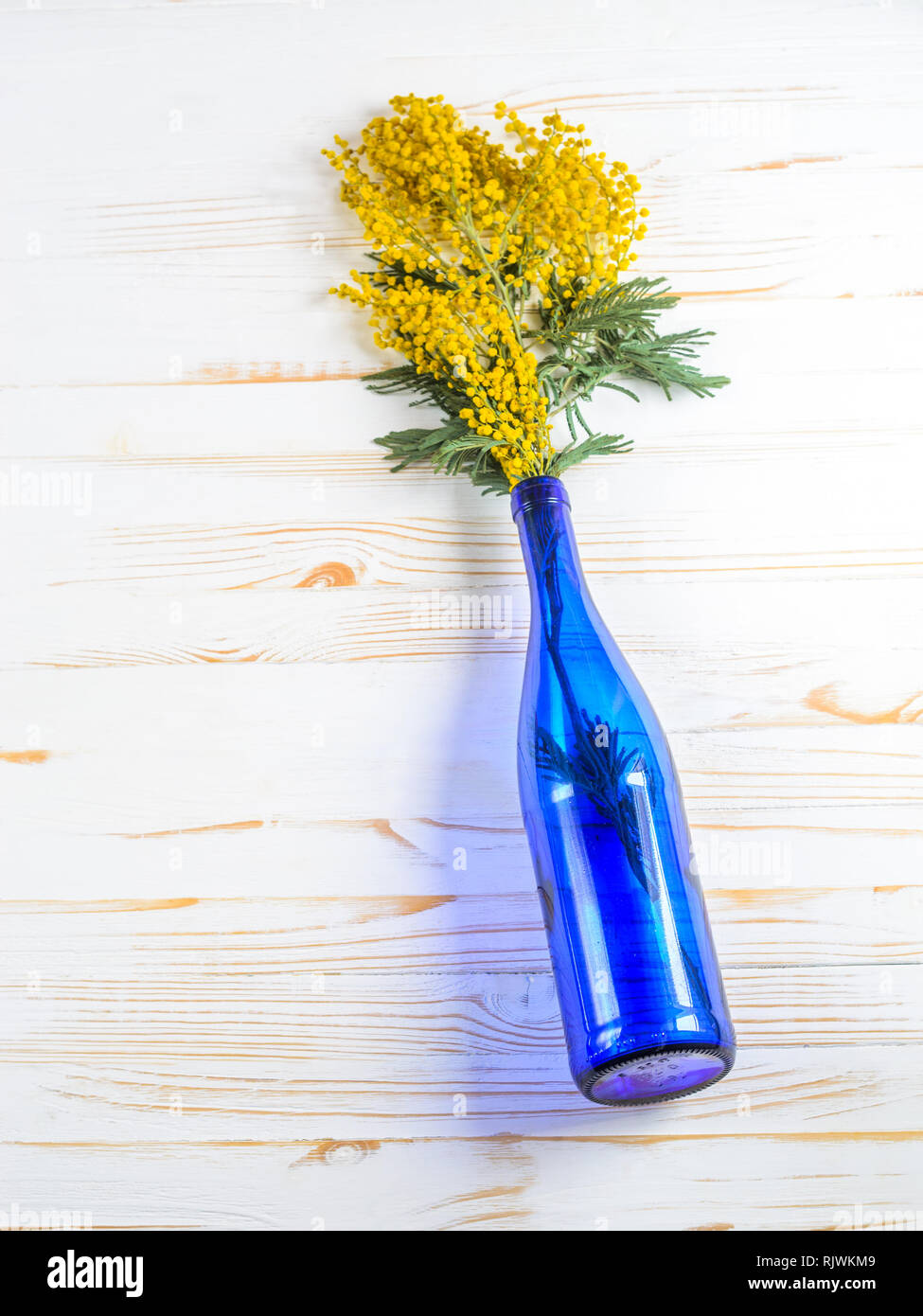 Mimosa Blumenstrauß in einer blauen Glasflasche auf weißem Holz Tisch Stockfoto