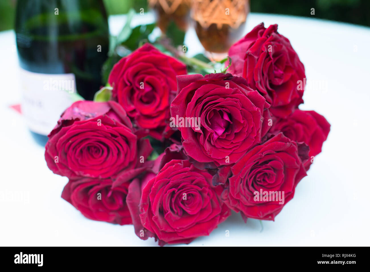 Rote Rosen Strauss Oder Das Bouquet Liegen Auf Weissen Tisch Im Freien Und Im Hintergrund Eine Flasche Champagner Oder Sekt Mit Zwei Glasern Gefullt Stockfotografie Alamy