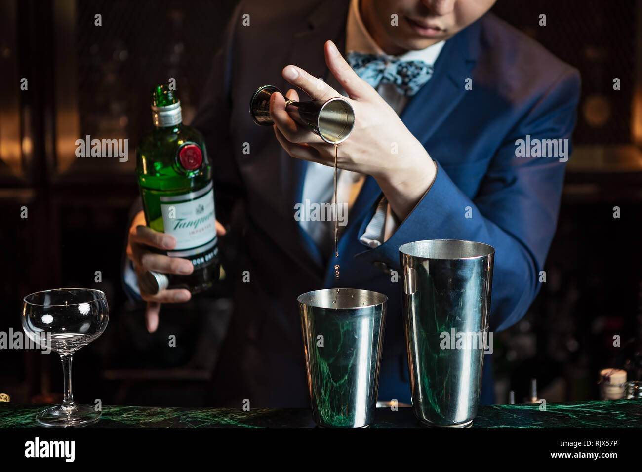 Der Barkeeper gießt Gin mit einer Jigger in den Blechschüttler Und den Cocktail vorbereiten Stockfoto