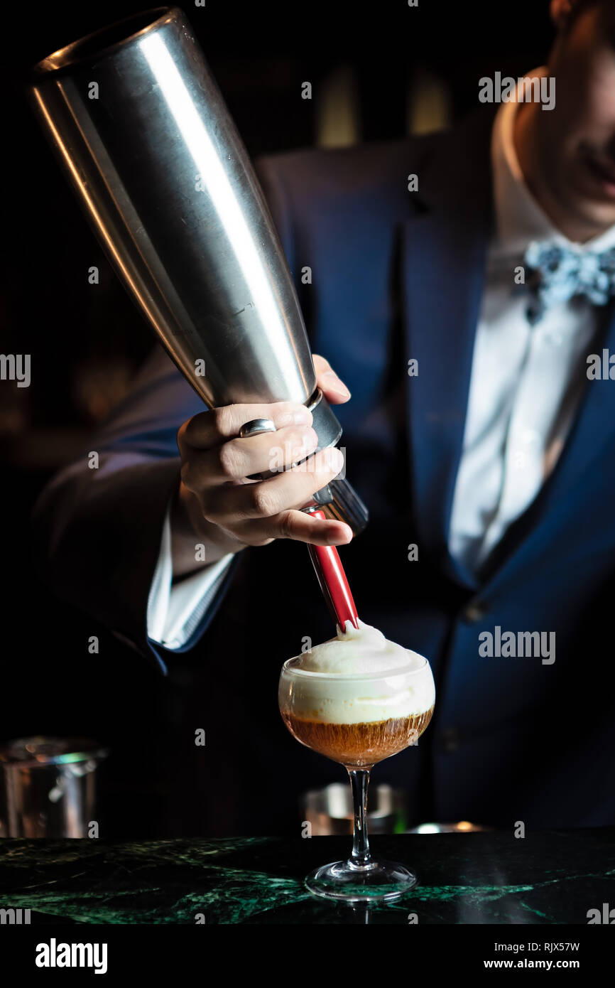 Der Barkeeper gibt den Schaum auf den fast fertigen Cocktail Stockfoto