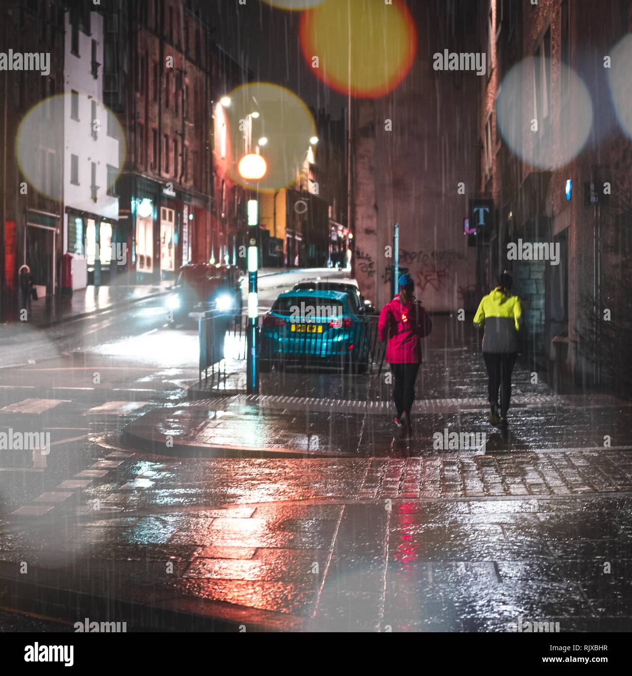 Zwei Damen, die während einer feuchten regnerischen Abend in den Straßen der Stadt von Edinburgh, Schottland. Der Regen fällt auf die Royal Mile und die Lichter der Stadt leuchten. Stockfoto