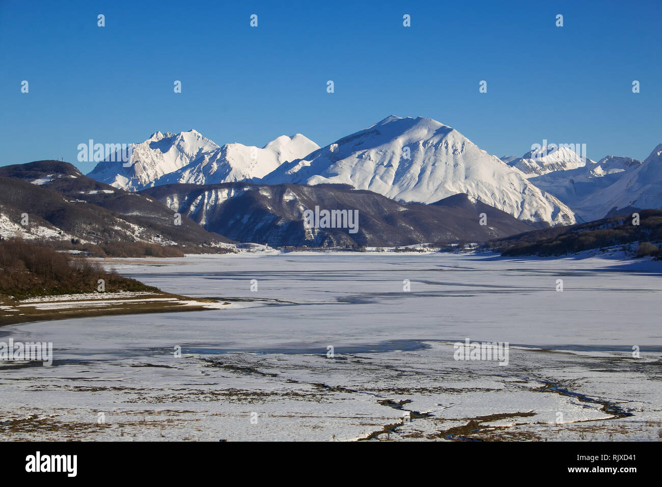 Gefrorene künstlicher Staudamm von Camposto mit hohen Bergen im Hintergrund, Abruzzen Stockfoto