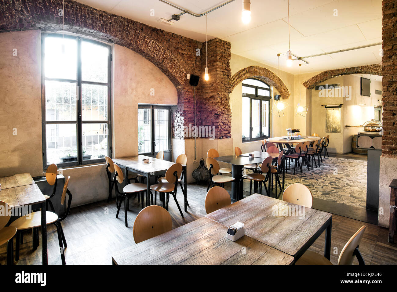 Tische und Stühle in einem leeren Restaurant im Landhausstil mit großen Bogenfenstern und viel Sonnenlicht Stockfoto