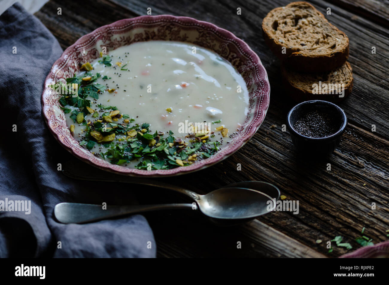 Schüssel mit Suppe. Es gibt Pistazien und Petersilie in die Suppe. Es ist in einem Vintage pink Platte auf einem braunen Holztisch. Horizontale zu Stockfoto