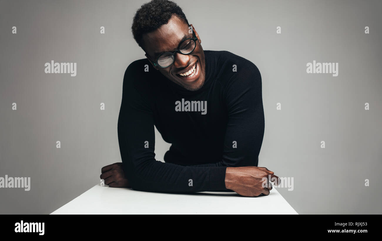 Afrikanischer mann am Tisch sitzen und Lächeln. Entspannt jungen Kerl gegen grauen Hintergrund. Stockfoto
