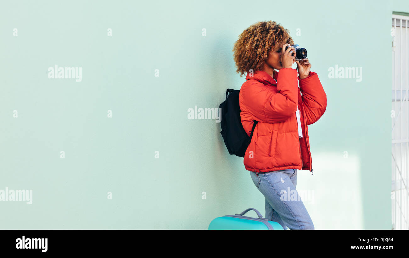Weibliche afro-amerikanischen Touristen stehen draußen mit ihrem Gepäck schiesst Fotos mit einer Digitalkamera. Frau auf Urlaub nimmt ein Foto stehen im Freien Stockfoto