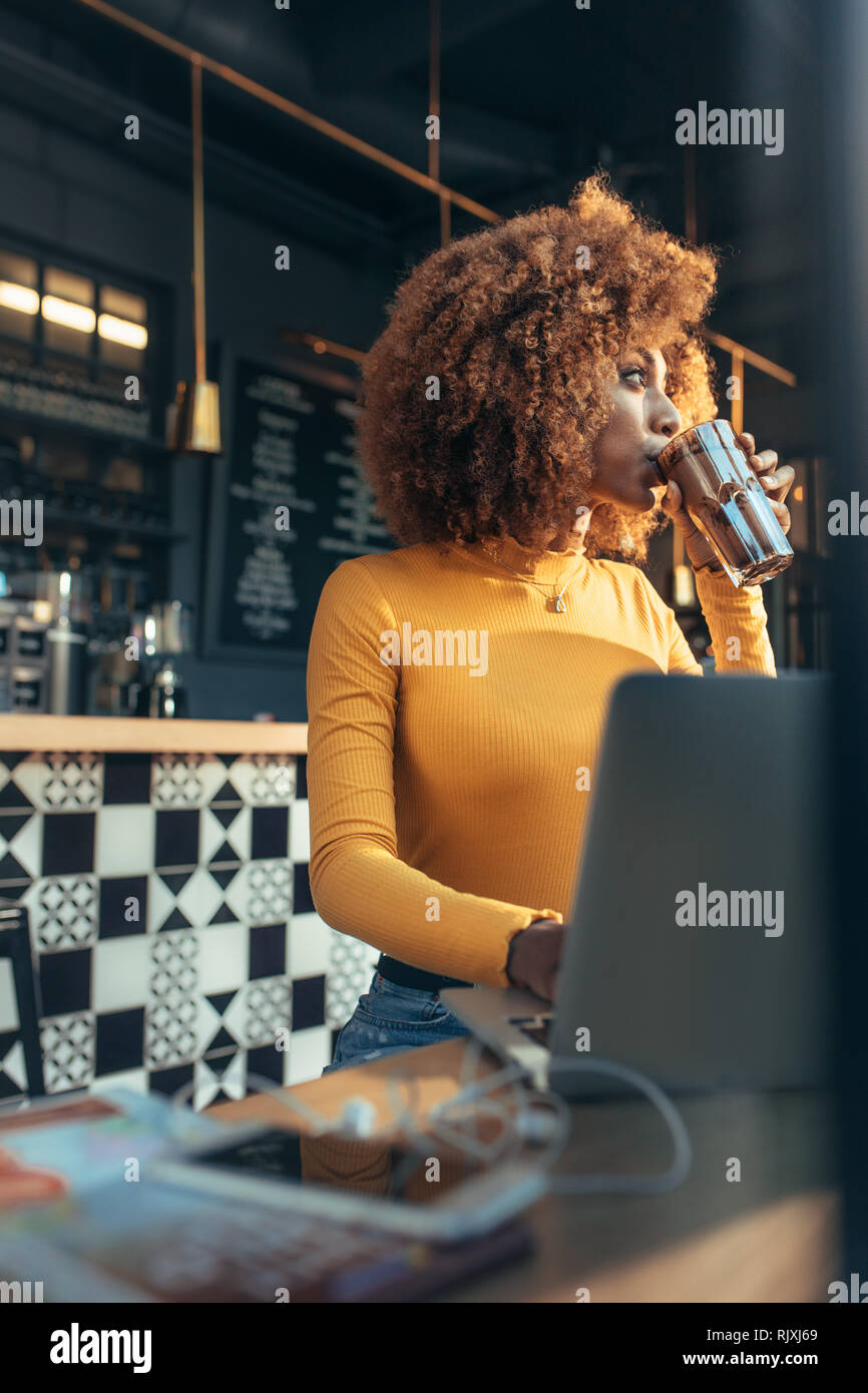 Frau Arbeiten am Laptop in einem Restaurant trinken Kaffee sitzen. Afro-amerikanische Frau genießen eine Tasse Schokolade schütteln während der Arbeit am Laptop in einem Ca Stockfoto