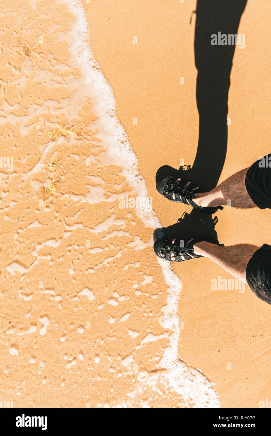 Hohe Betrachtungswinkel von Mans Füße paddeln durch Wasser am Strand, vertikal Stockfoto
