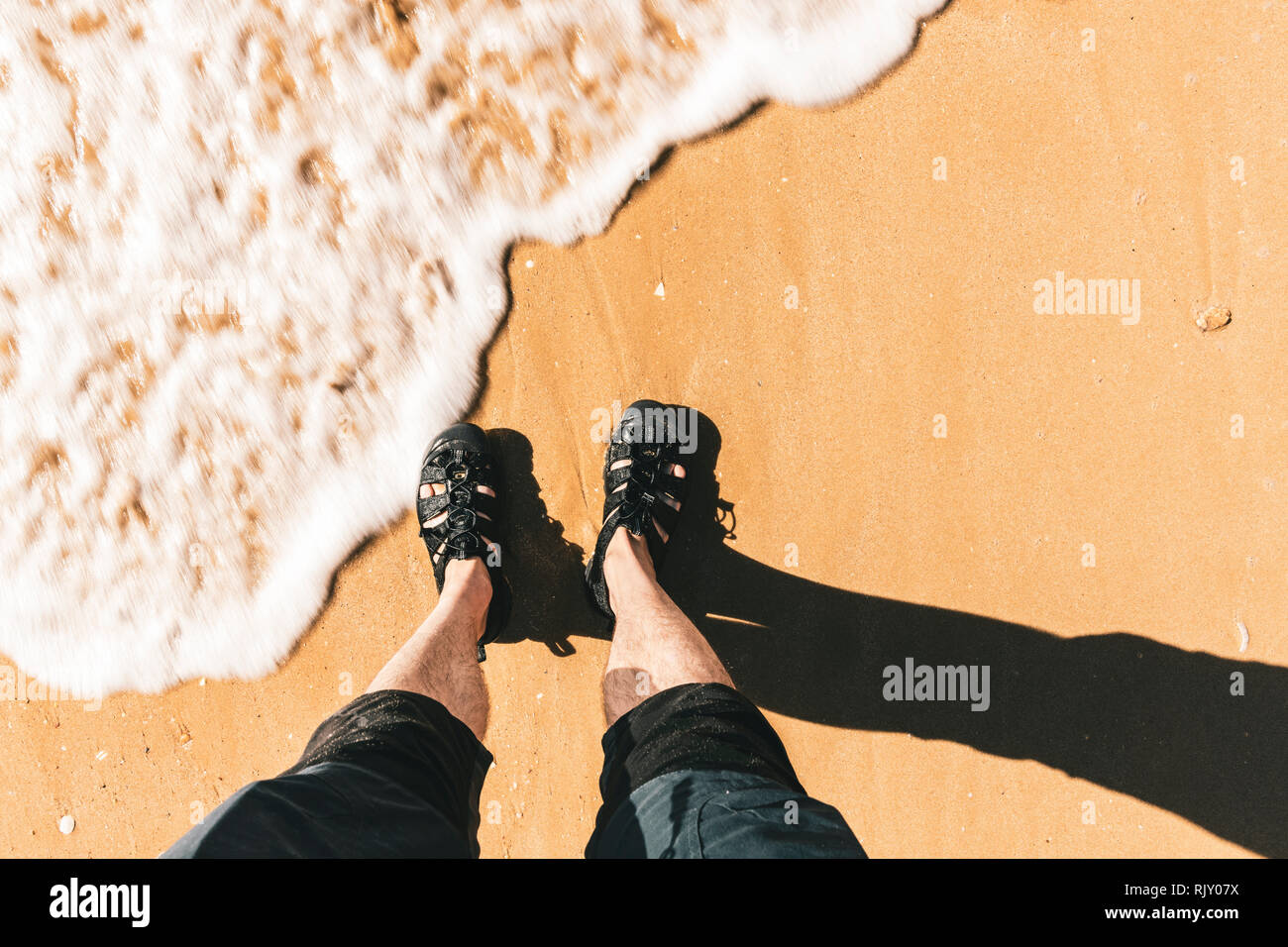 Hohe Betrachtungswinkel von Mans Füße paddeln durch Wasser am Strand, horizontal Stockfoto