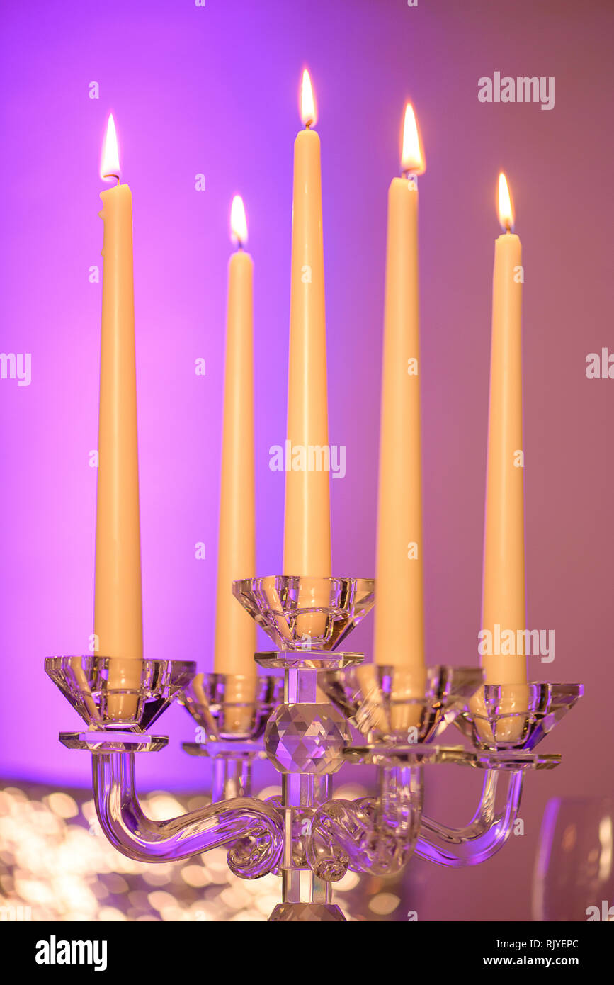 Fünf lange brennende Kerzen in einem schönen Kristall Kerzenhalter set mit fünf Scalloped bobeche, vertikale Perspektive gegen eine weiche Lila Stockfoto