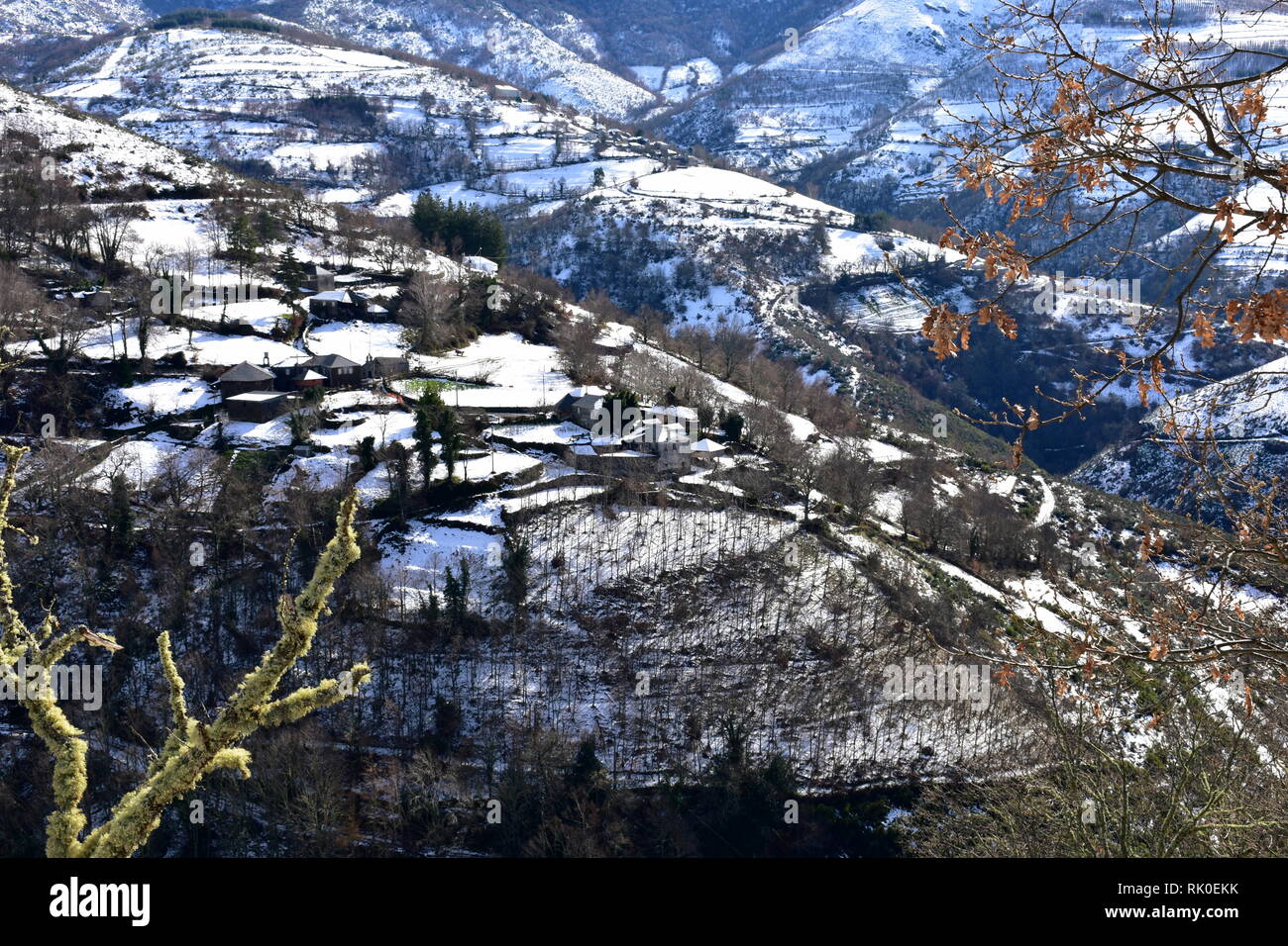 Kleines Bergdorf auf einem schneebedeckten Hang mit Bäumen. Ancares Region, Provinz Lugo, Galizien, Spanien. Stockfoto