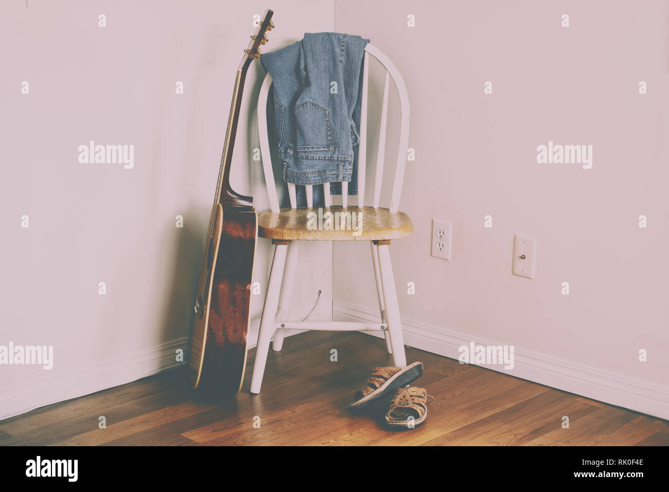 BlueJeans hängen an der Rückseite des leeren Stuhl mit Sandalen am Boden und Akustik Gitarre. Stockfoto