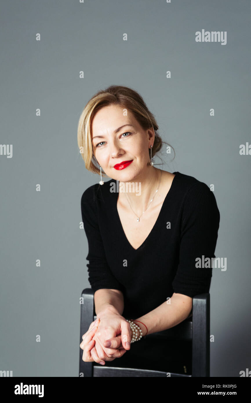 Porträt der schönen Frau in einem schwarzen Kleid vor grauem Hintergrund Stockfoto