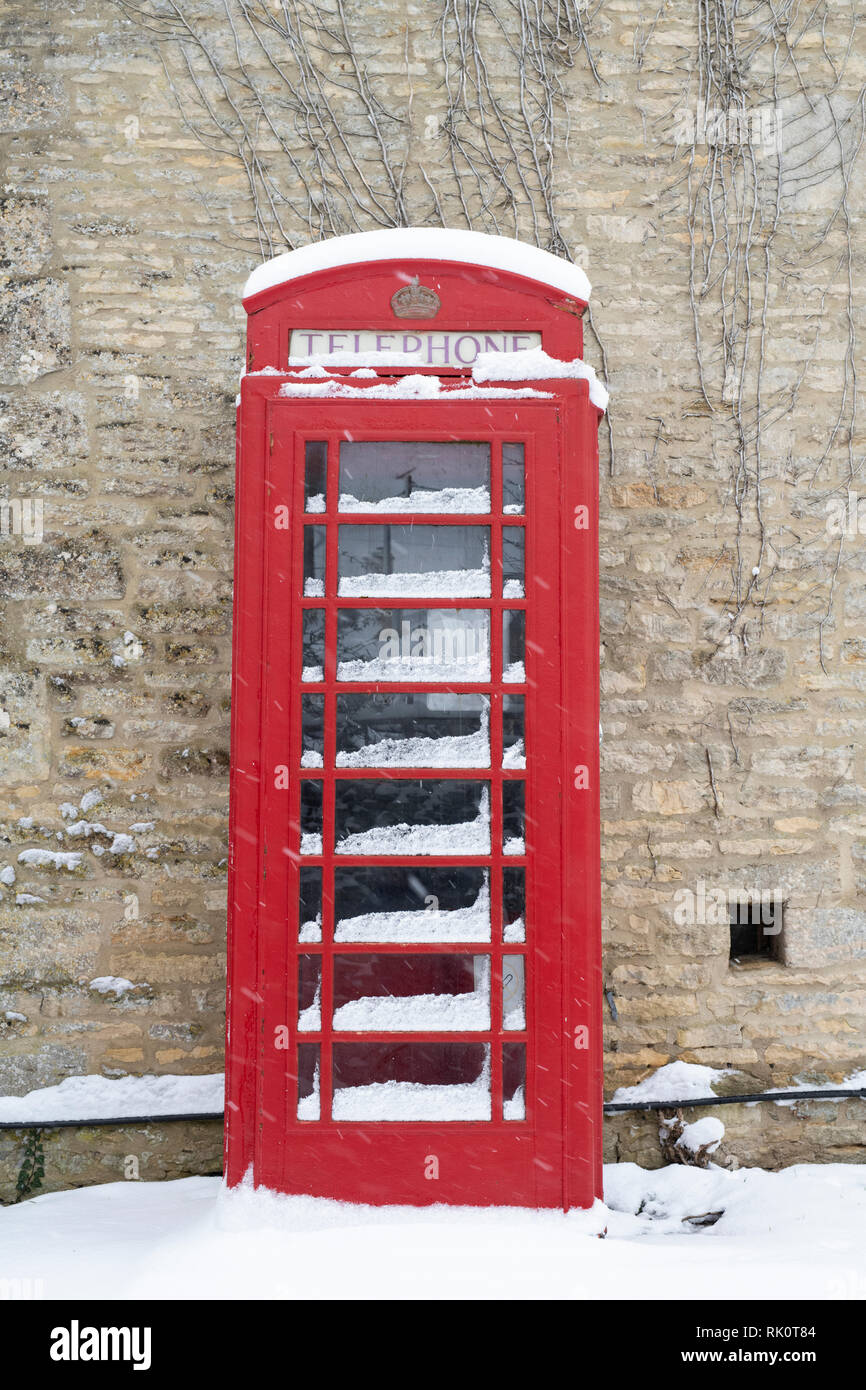 Rote Telefonzelle in Winson Dorf im Winter Schnee. Winson, Cotswolds, Gloucestershire, England Stockfoto
